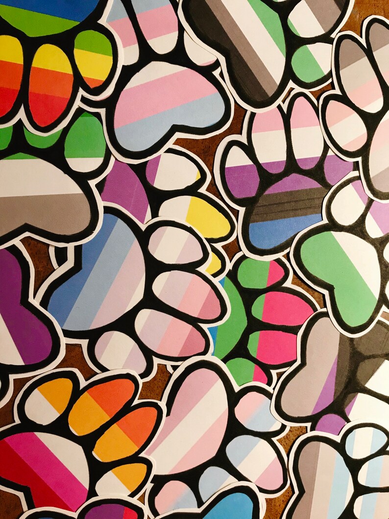 May include: A collection of paw print stickers with various pride flag colors, including rainbow, transgender, bisexual, and genderqueer.