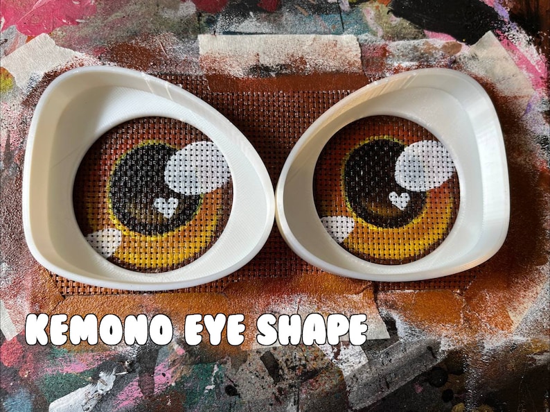 May include: Two white plastic eye shape templates for crafting. The templates are shaped like an almond with a rounded edge. The text "Kemon Eye Shape" is printed below the templates.