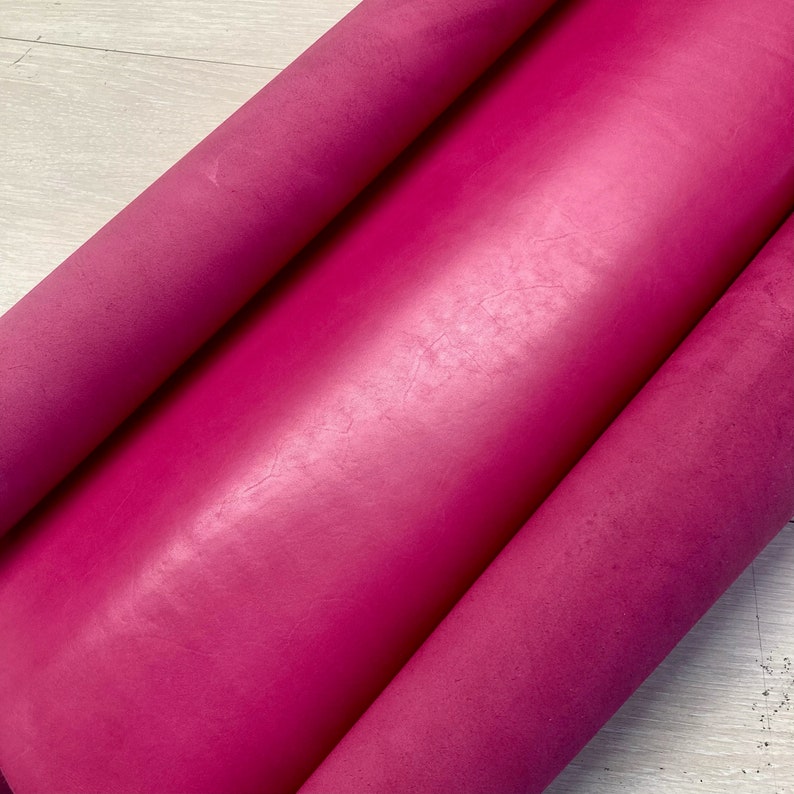 May include: Close-up of a bright pink leather material rolled up. The leather has a smooth, slightly textured surface.