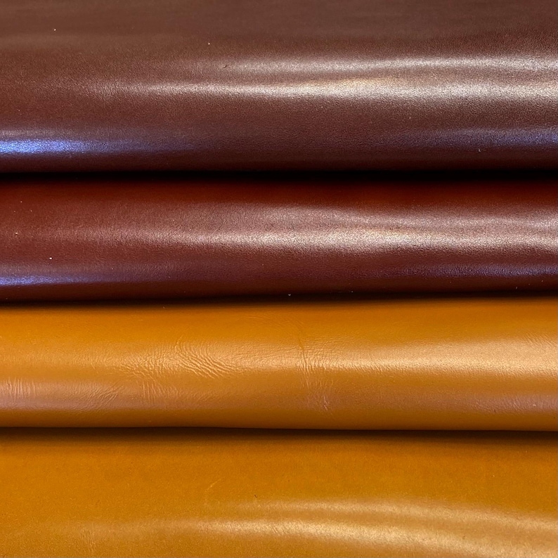 May include: Close-up of three leather samples in varying shades. The top is a dark burgundy, the middle a mid-brown, and the bottom a warm, golden-yellow. The leather has a smooth texture and a subtle sheen, indicating a quality finish.