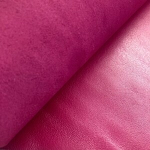 May include: Close-up of a vibrant magenta leather fabric with a smooth, shiny finish on one side and a textured, matte finish on the other side.
