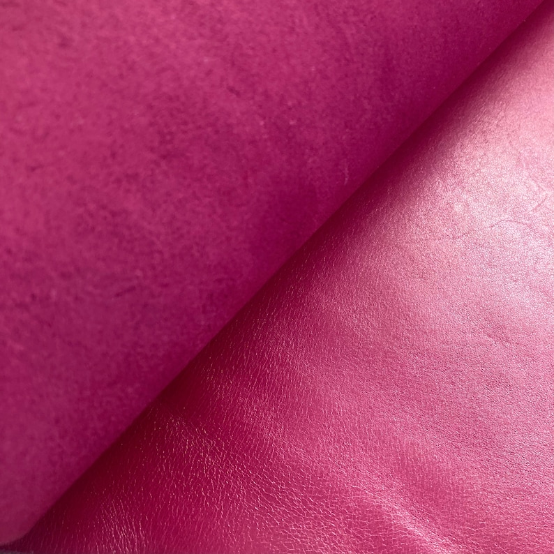 May include: Close-up of a vibrant magenta leather fabric with a smooth, shiny finish on one side and a textured, matte finish on the other side.