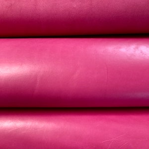 May include: Close-up of three rolls of pink leather. The leather has a smooth, shiny finish.