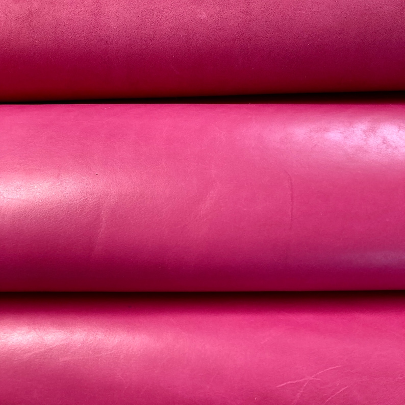 May include: Close-up of three rolls of pink leather. The leather has a smooth, shiny finish.