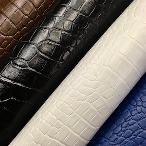 Könnte beinhalten: Nahaufnahme von vier verschiedenen Krokodilprägungen aus Leder. Die Muster sind in einer Reihe angeordnet, wobei das braune Muster oben liegt, gefolgt von Schwarz, Weiß und Blau.
