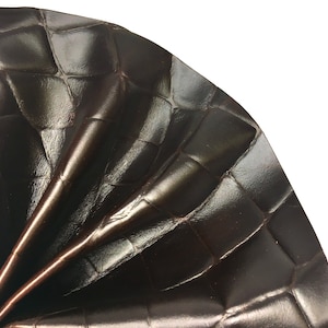 Puede incluir: Primer plano de un material de cuero marrón oscuro con un patrón en relieve de cocodrilo. El cuero está doblado y texturizado, mostrando los intrincados detalles del diseño.