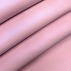 Pode incluir: Um tecido rosa claro sólido com uma textura lisa e mate, dobrado em três camadas horizontais distintas. O material apresenta um tom rosa pastel consistente em toda a sua superfície, com sombras suaves criadas pelas dobras do tecido.