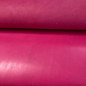 May include: Close-up of a smooth, deep pink leather material. The leather has a subtle sheen and a slightly textured surface.
