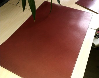 May include: A brown leather desk mat with stitched edges. The mat is on a light wood desk.