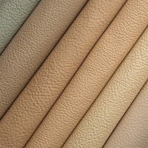 May include: Close-up of a textured leather fabric in various shades of brown, beige, and cream. The leather is arranged in diagonal strips, creating a pattern of overlapping lines.
