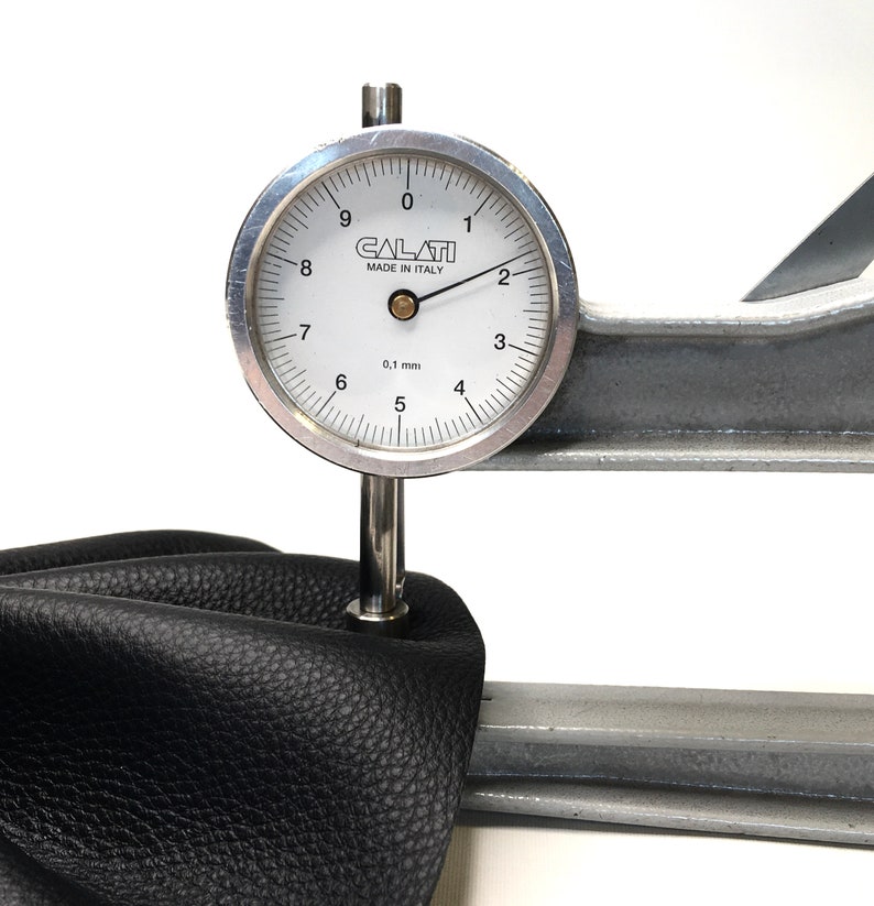 May include: A close-up of a leather sample being tested with a dial gauge. The gauge reads 0.1 mm and is labeled "CALATI MADE IN ITALY".