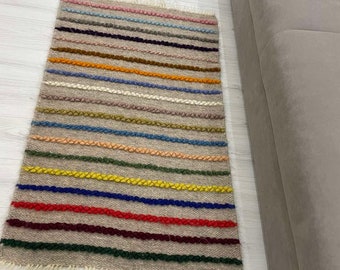 May include: A beige woven rug with colorful stripes. The stripes are made of braided yarn in various colors, including red, blue, yellow, green, and pink.