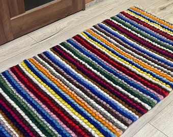 May include: A colorful striped rug with a textured, fluffy surface. The rug is made of wool and has a variety of colors, including red, blue, yellow, green, and white.