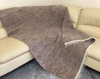 May include: A brown and white striped wool throw blanket with a fringe edge is draped over a cream colored couch.