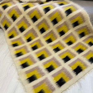 May include: A white, yellow and black patterned throw blanket with a fuzzy texture. The blanket has a geometric design with squares and a fringed edge.