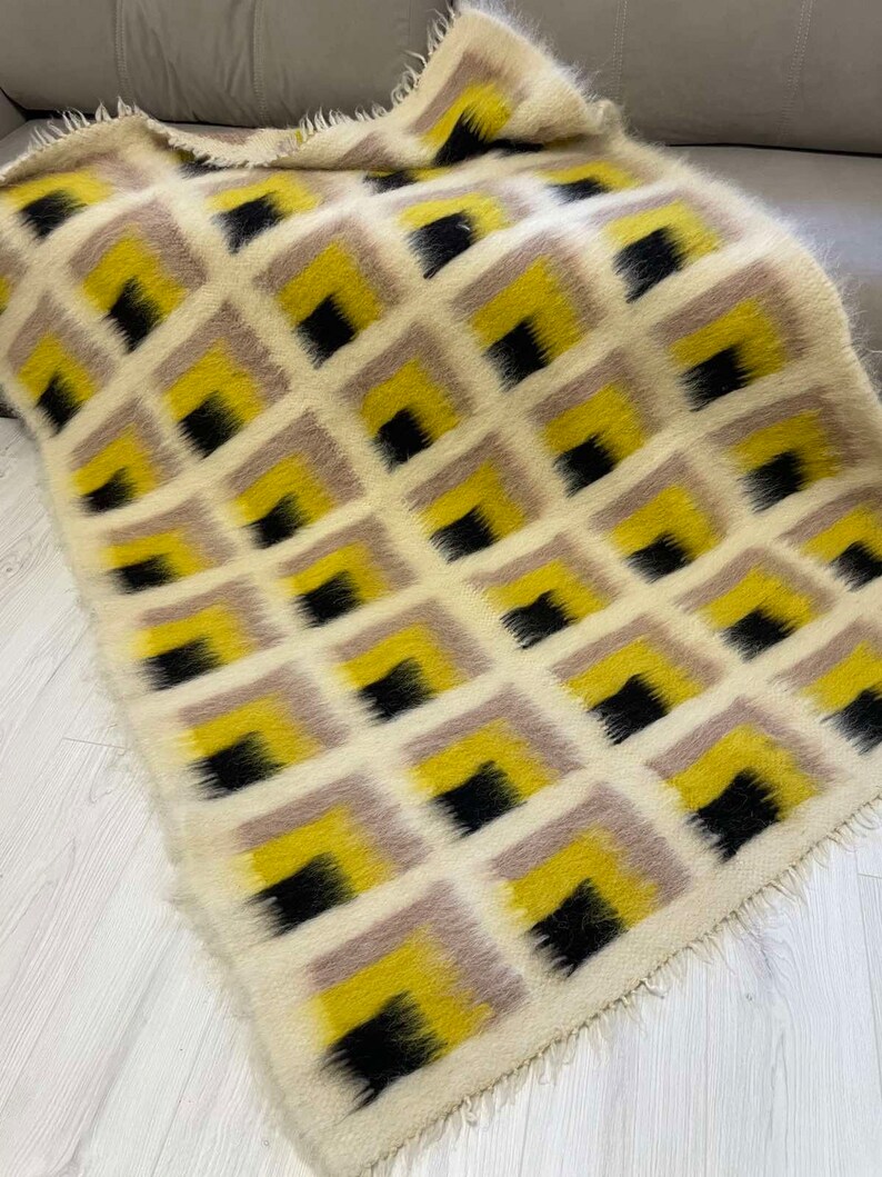 May include: A white, yellow and black patterned throw blanket with a fuzzy texture. The blanket has a geometric design with squares and a fringed edge.