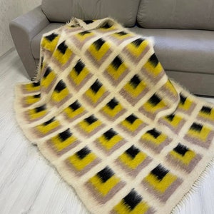 May include: A soft, fluffy throw blanket with a geometric pattern of black, yellow and beige squares. The blanket has a fringed edge.