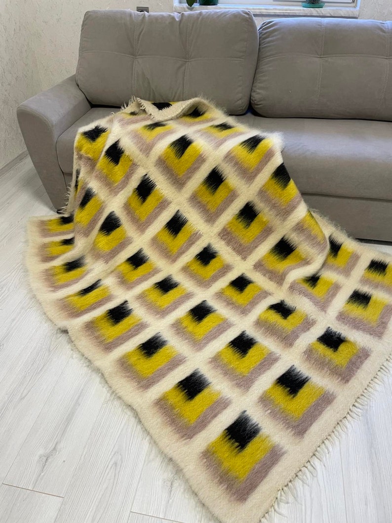 May include: A soft, fluffy throw blanket with a geometric pattern of black, yellow and beige squares. The blanket has a fringed edge.