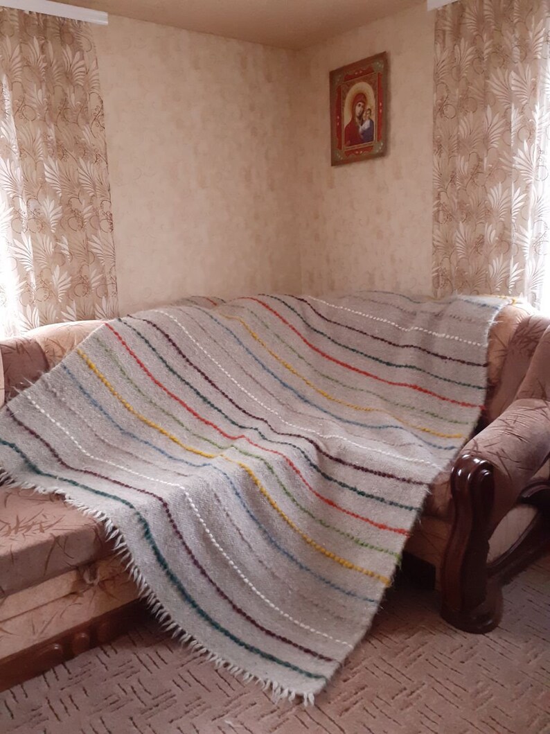 May include: A striped throw blanket with a fringed edge, draped over a sofa. The blanket is made from a soft, natural fibre and features a range of colours, including beige, brown, green, yellow, and red.