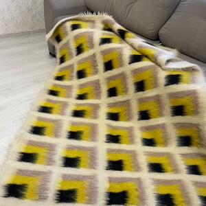May include: A white, black and yellow geometric patterned throw blanket with a fringe border. The blanket is draped over a grey sofa.