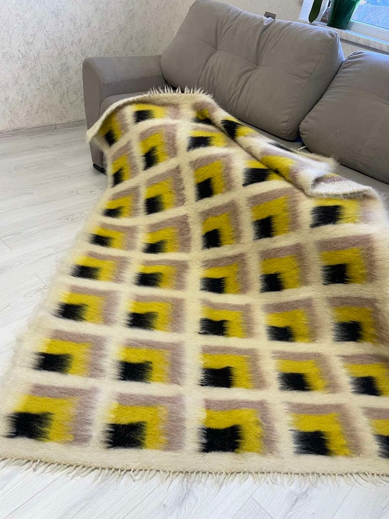 May include: A white, black and yellow geometric patterned throw blanket with a fringe border. The blanket is draped over a grey sofa.