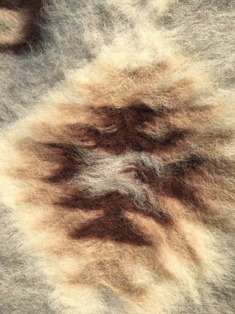 Pode incluir: Close-up de um tecido texturizado marrom, branco e cinza com uma apar&ecirc;ncia felpuda e macia.