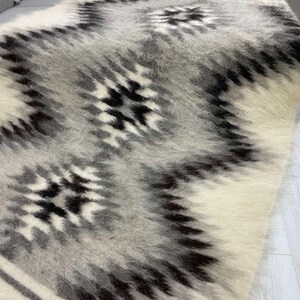 May include: A soft, textured rug with a geometric pattern. The rug features a repeating design of black and gray shapes against a white and light gray background. The rug is made of a fluffy material.