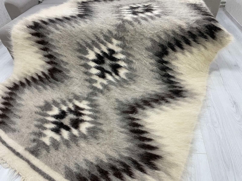 May include: A soft, textured rug with a geometric pattern. The rug features a repeating design of black and gray shapes against a white and light gray background. The rug is made of a fluffy material.
