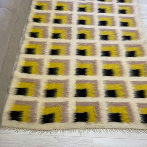 May include: A white, yellow and black geometric patterned rug with a fringe border. The rug has a modern design with squares and rectangles.