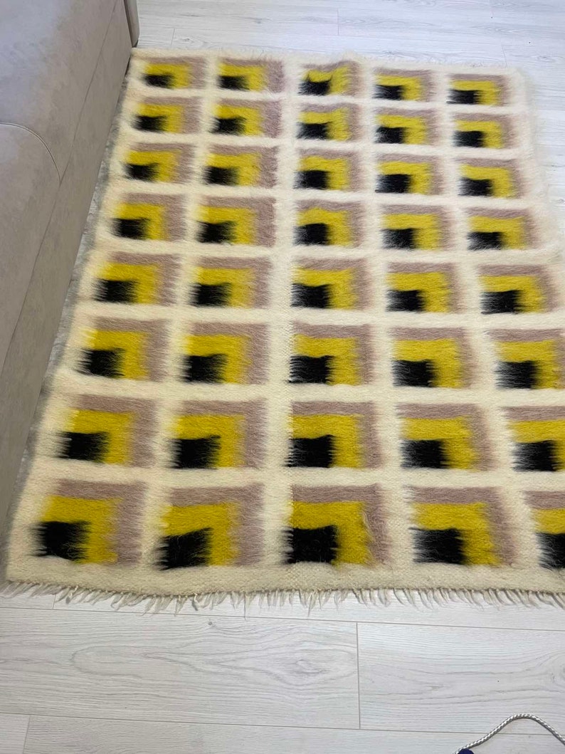 May include: A white, yellow and black geometric patterned rug with a fringe border. The rug has a modern design with squares and rectangles.