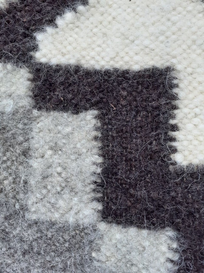 Pode incluir: Close-up de um tapete tecido com um padr&atilde;o geom&eacute;trico em preto e branco. O tapete tem uma textura felpuda e &eacute; feito de l&atilde;.