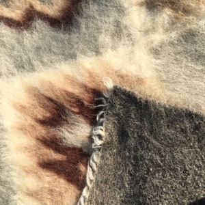 Pode incluir: Close-up de um cobertor macio e felpudo com um esquema de cores castanho, bege e cinzento. O cobertor tem um aspeto tecido texturizado e parece muito aconchegante.