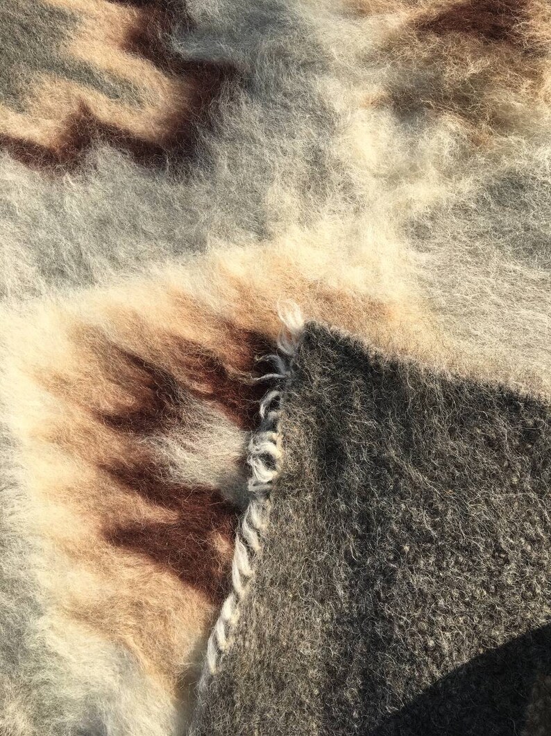 Pode incluir: Close-up de um cobertor macio e felpudo com um esquema de cores castanho, bege e cinzento. O cobertor tem um aspeto tecido texturizado e parece muito aconchegante.