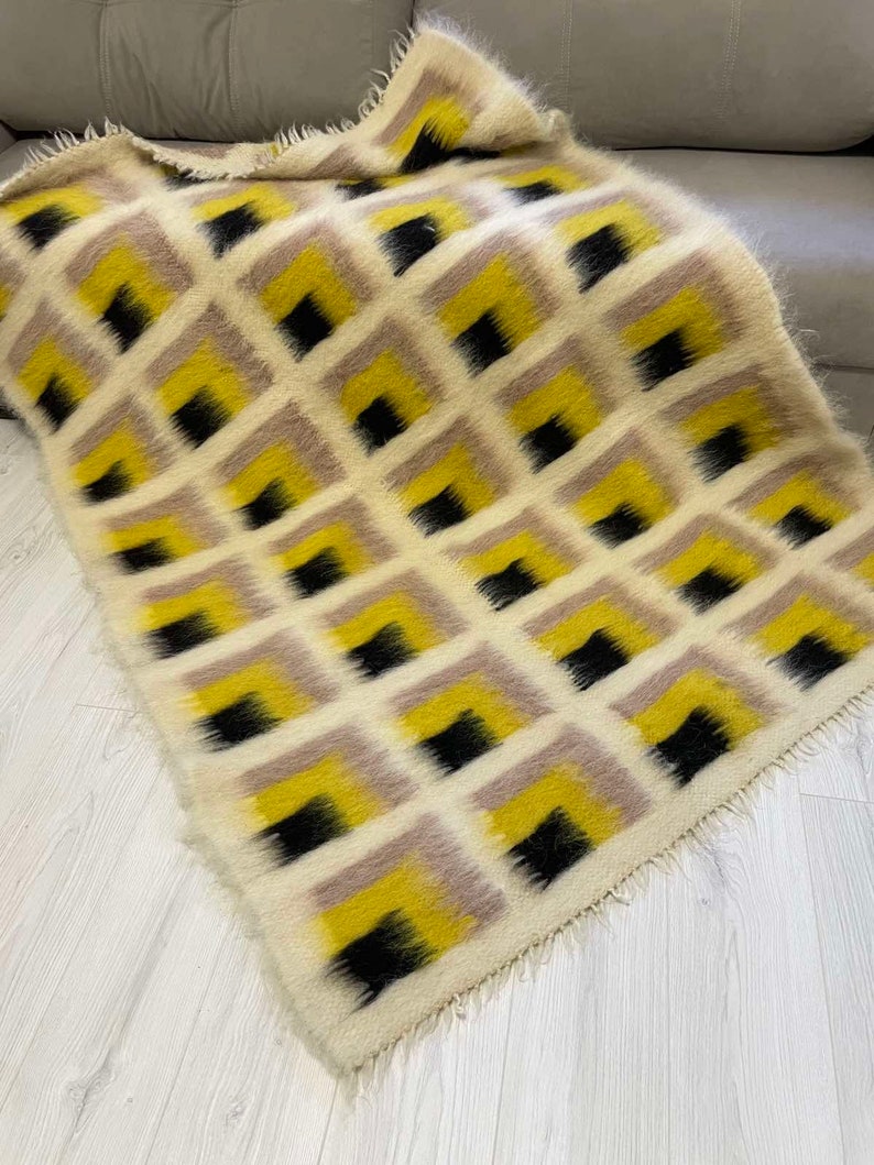 May include: A white, yellow and black geometric patterned throw blanket with a fringed edge.