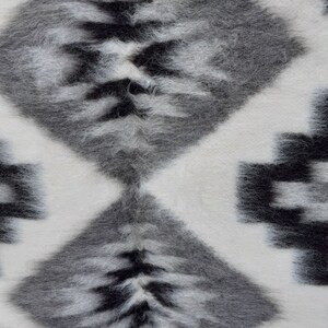 Pode incluir: Um tapete com padr&atilde;o branco e preto com textura felpuda. O tapete tem um padr&atilde;o de diamante com listras pretas e brancas.