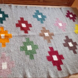 Puede incluir: Una alfombra de lana gris con un patr&oacute;n geom&eacute;trico de cuadrados coloridos. Los cuadrados son en tonos de verde, rojo, naranja, amarillo, rosa, marr&oacute;n y turquesa.