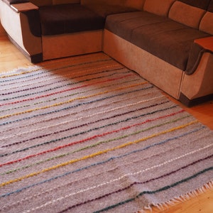 May include: A grey and white striped rug with colourful accents. The rug has a fringed border and is made of a soft, textured material.
