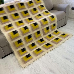 May include: A white, yellow and black patterned throw blanket with a fringe border. The blanket is draped over a grey sofa.