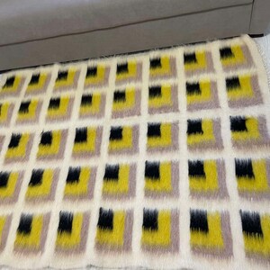 May include: A white, fluffy rug with a geometric pattern of black, yellow, and beige squares.