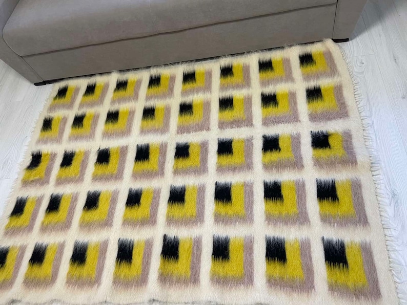 May include: A white, fluffy rug with a geometric pattern of black, yellow, and beige squares.