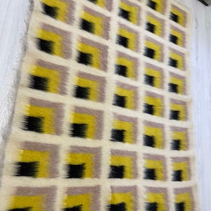 May include: A white, yellow and black geometric patterned rug with a fringed edge. The rug is made of wool and has a modern design.