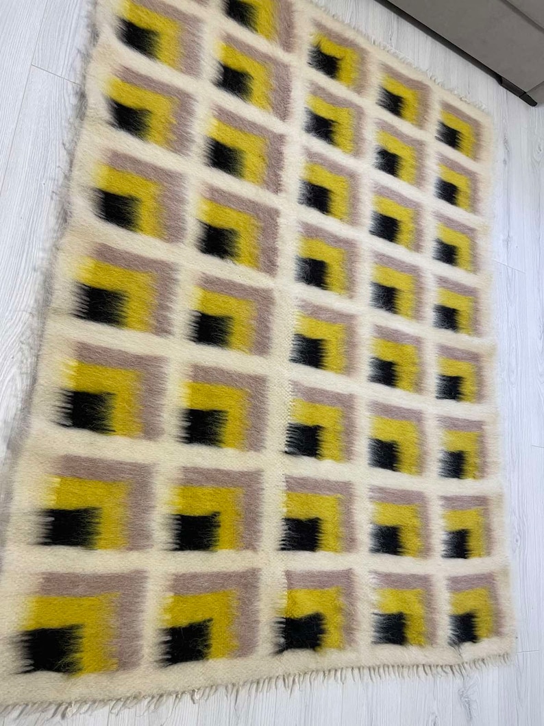 May include: A white, yellow and black geometric patterned rug with a fringed edge. The rug is made of wool and has a modern design.