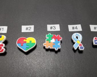 May include: Five colorful charms with autism awareness themes. The charms include the word "LOVE" with a puzzle piece heart, a puzzle piece heart, a puzzle piece, a blue ribbon, and a charm that says "AUTISM FRIENDLY".