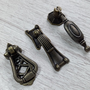 Può includere: Tre tiretti per mobili in stile antico con finitura bronzo. I tiretti hanno disegni decorativi e sono realizzati in metallo.