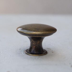 May include: A bronze cabinet knob with an oval head and a short, rounded stem. The knob has a vintage appearance, with a slightly textured surface and a dark, aged finish. Suitable for furniture and cabinet hardware.
