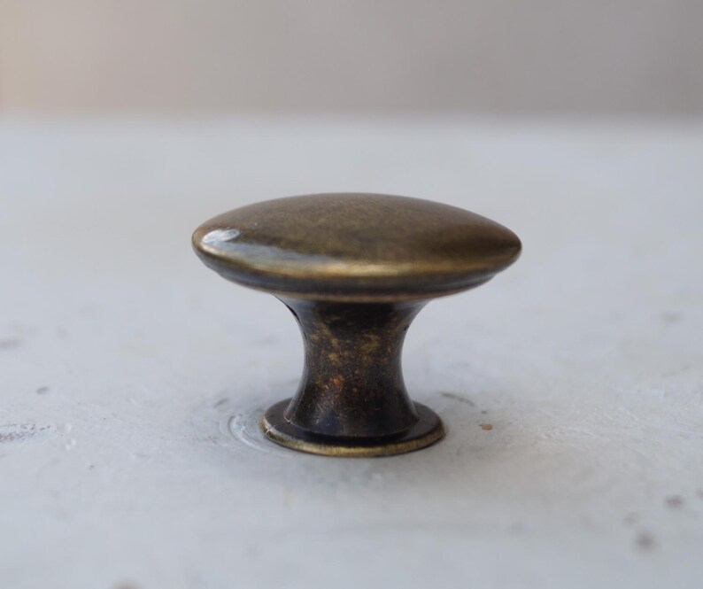 May include: A bronze cabinet knob with an oval head and a short, rounded stem. The knob has a vintage appearance, with a slightly textured surface and a dark, aged finish. Suitable for furniture and cabinet hardware.