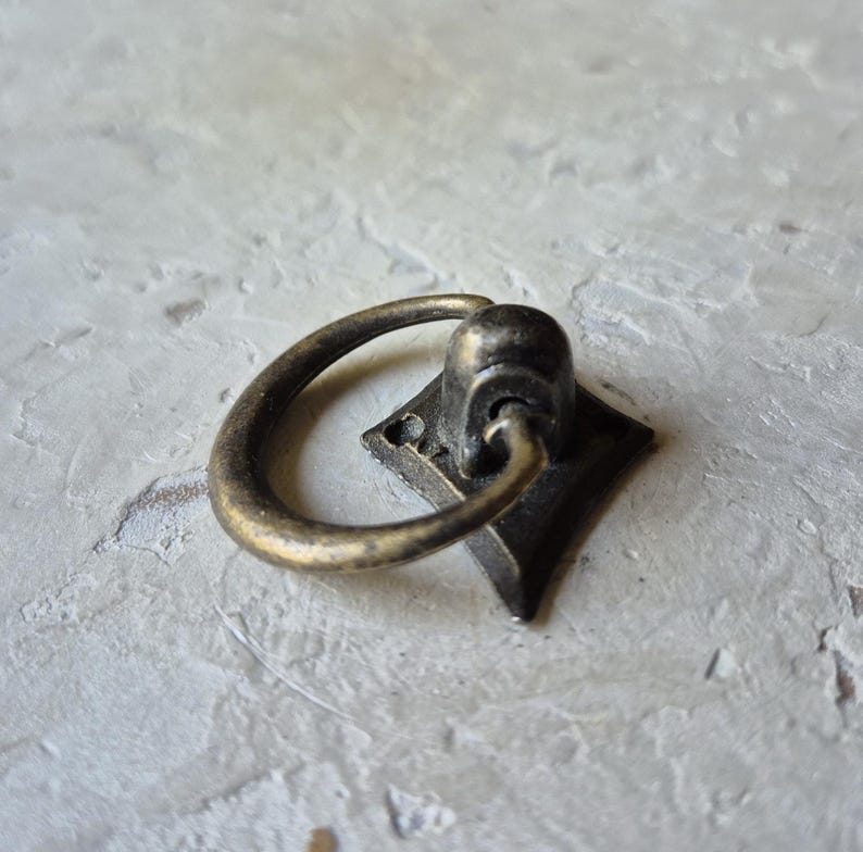 May include: Antique brass drawer pull with a diamond-shaped base and a curved handle. The hardware has a vintage aesthetic, perfect for adding a touch of classic style to furniture or cabinetry. The pull is made of metal.