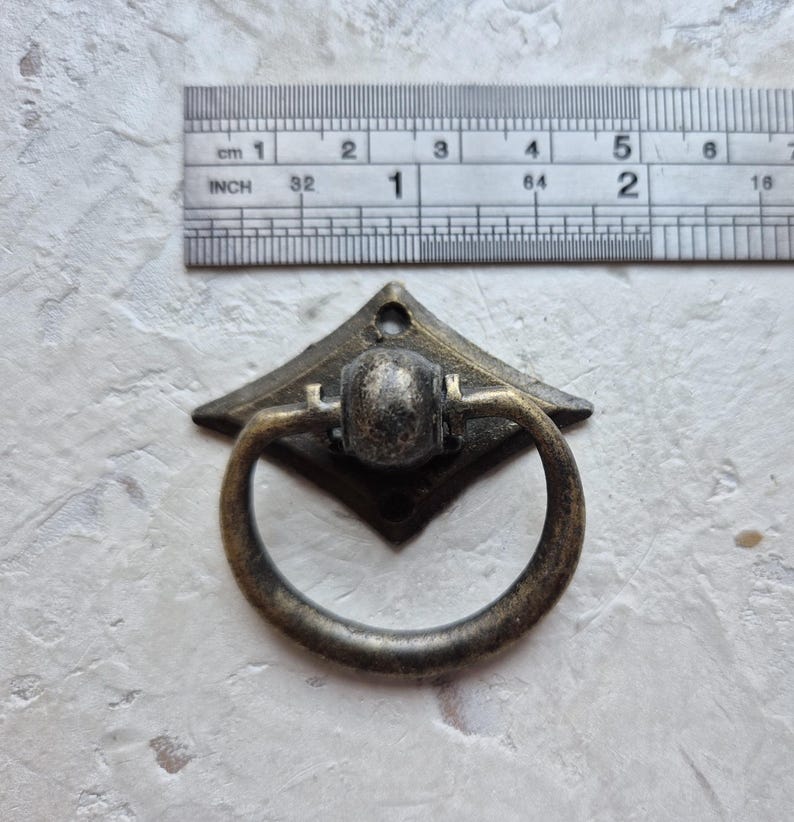 May include: Antique bronze drawer pull with a diamond-shaped backplate and a circular handle. The pull measures approximately 1 inch in width. The hardware has a vintage aesthetic, suitable for cabinets, drawers, or furniture restoration projects.