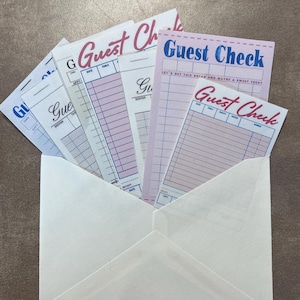 May include: A white envelope containing several guest check pads. The pads have a variety of pastel colors, including pink and blue, with the words "Guest Check" in a decorative font. The checks have spaces for date, table, and server information.