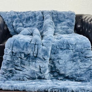 May include: A plush, blue faux fur throw blanket draped over a black leather armchair. A wooden acoustic guitar leans against the wall to the left of the chair, creating a cozy, inviting scene.